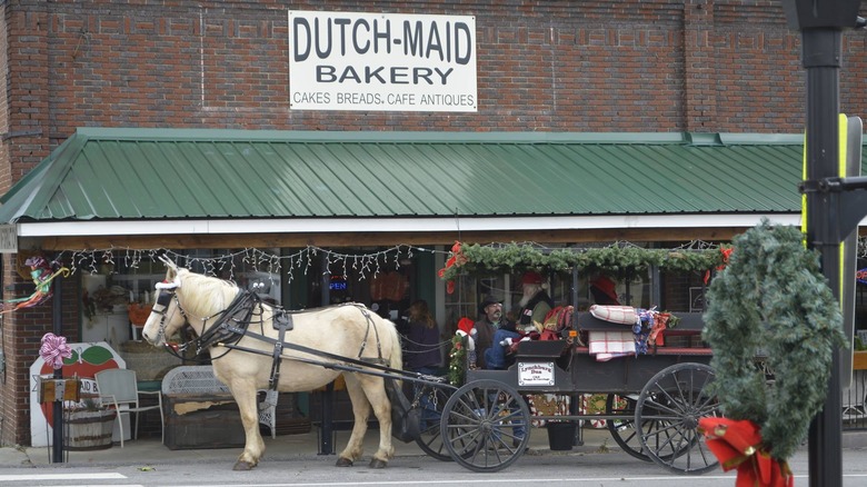 image of Dutch Maid Bakery storefront decorated for Christmas with a white horse in front pulling a carriage