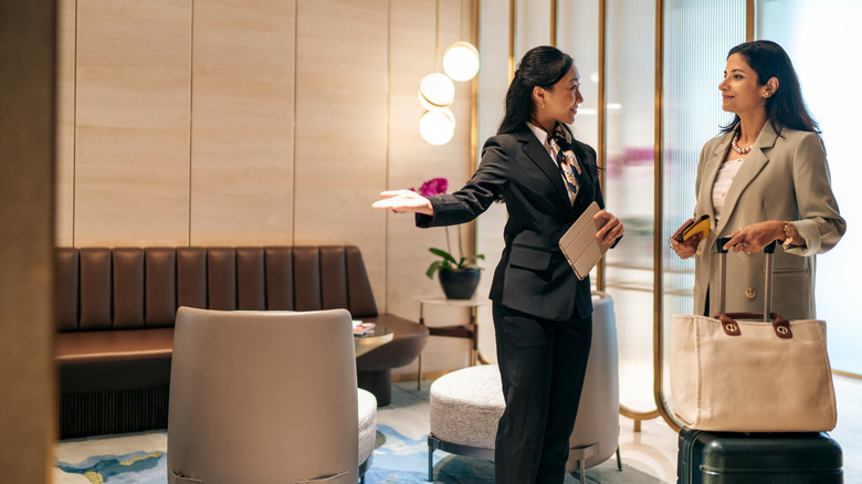 White-gloved airport attendant ushering in a woman holding a bag and luggage