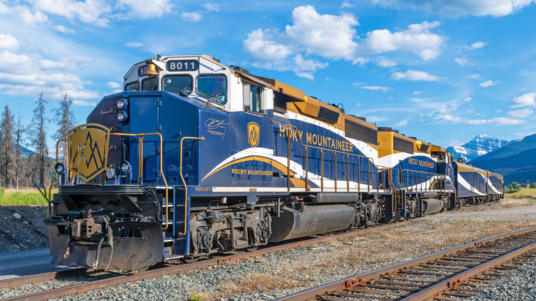 Rocky Mountaineer train on a sunny day traveling on a train track with mountains in the background