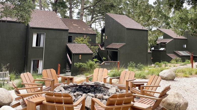 A fire pit surrounded by adirondack chairs in front of cabins