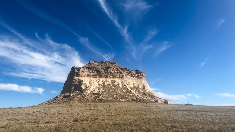 A butte against the blue sky and clouds, with grasslands
