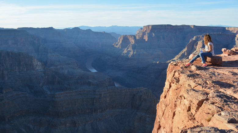 A woman on the edge of the Grand Canyon with the river below