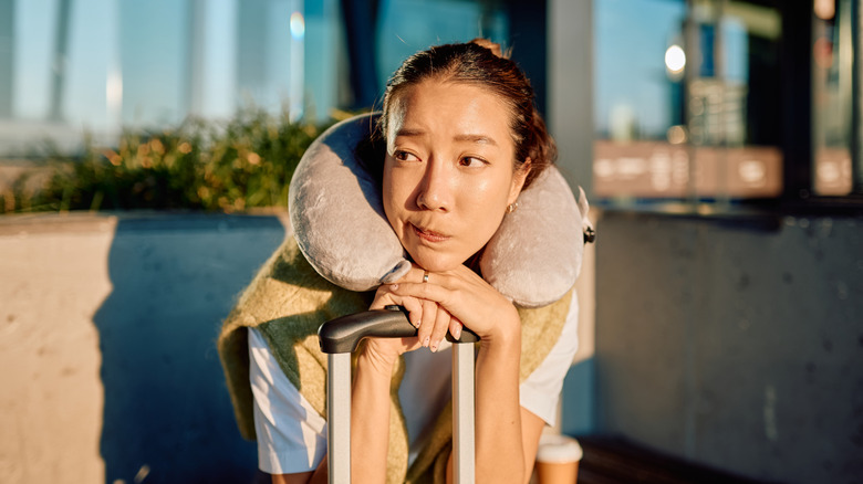 An uncertain traveler leaning on luggage handle