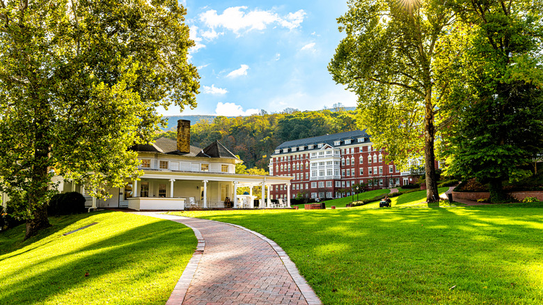 White heritage building with columns in front of red-brick historic building in grassy lawn framed by leafy trees in Bath County, Virginia