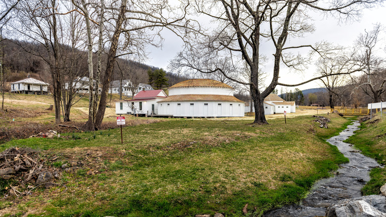 Round bathhouse with white walls in a grassy field with a small stream flowing in Bath County, Virginia