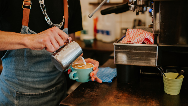 A barista pouring a latte into a cup