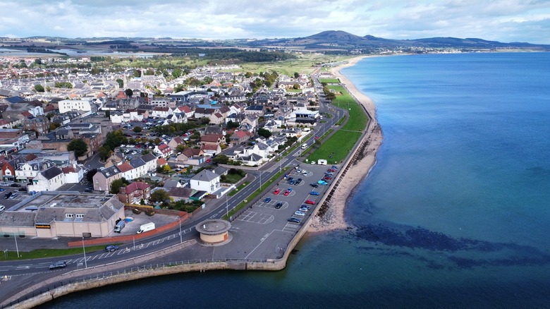 An aerial photo of Leven with the clear blue waters meeting the sandy strip of beach and the small village behind