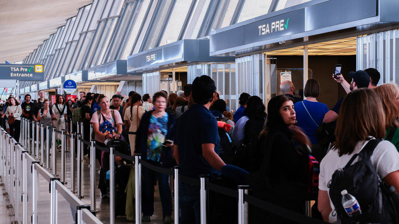a large group of travelers wait in a long line to enter the security checkpoint