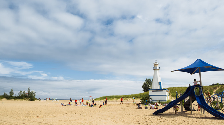 People on the beach in New Buffalo, with a playground and replica lighthouse in the foreground