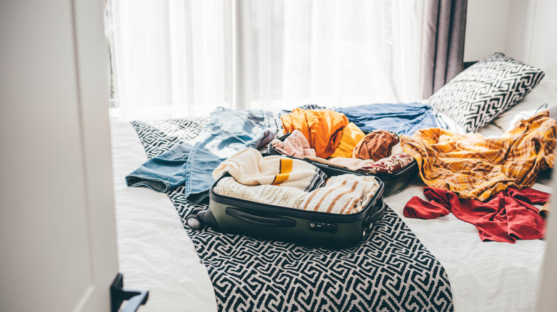 Clothes on a hotel bed, some in the suitcase, some tossed about.