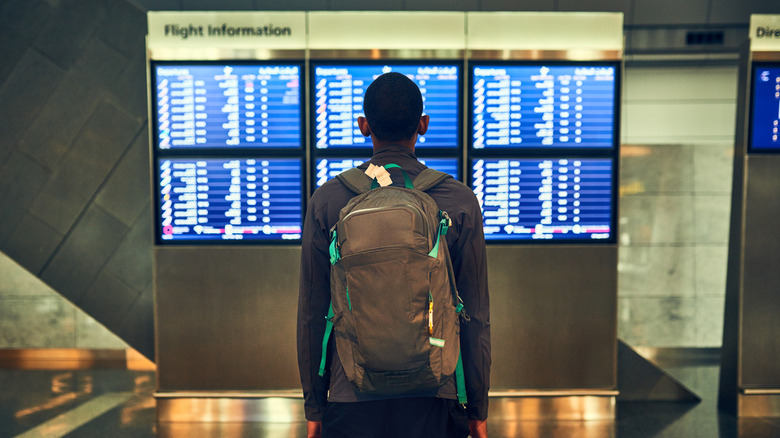 Man standing in front of flight roster board in airport