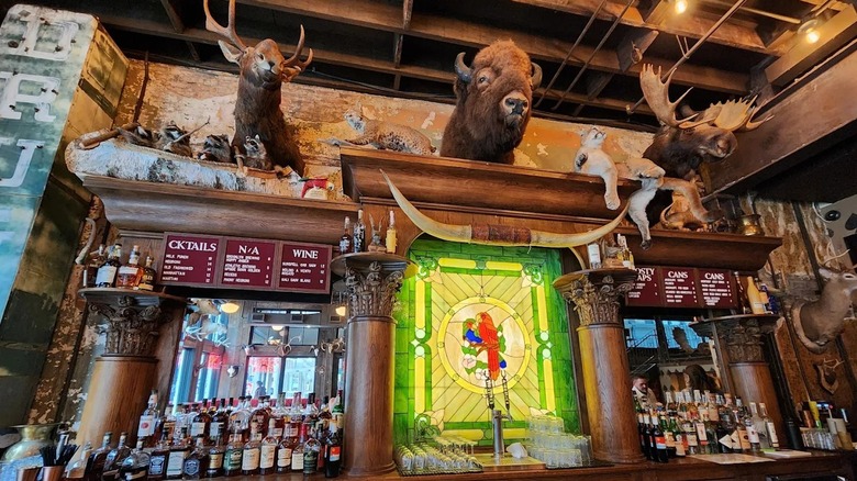An ornate wooden bar with stained glass and hanging taxidermied moose heads