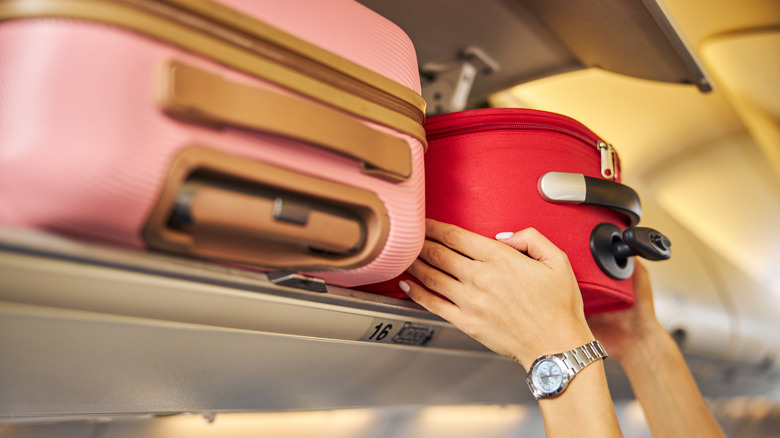Hands placing a suitcase in an overhead baggage compartment
