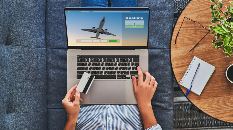Overhead shot of a man purchasing flights on his computer, with a notepad, pen, and his credit card at the ready