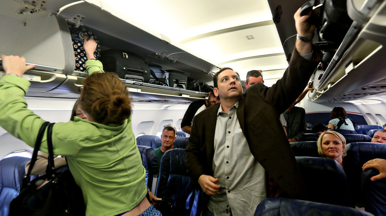 People putting luggage into overhead compartment