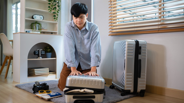 Man kneeling on overpacked suitcase to close it