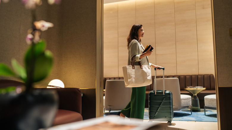 A woman walking into an airport lounge rolling her carry-on luggage