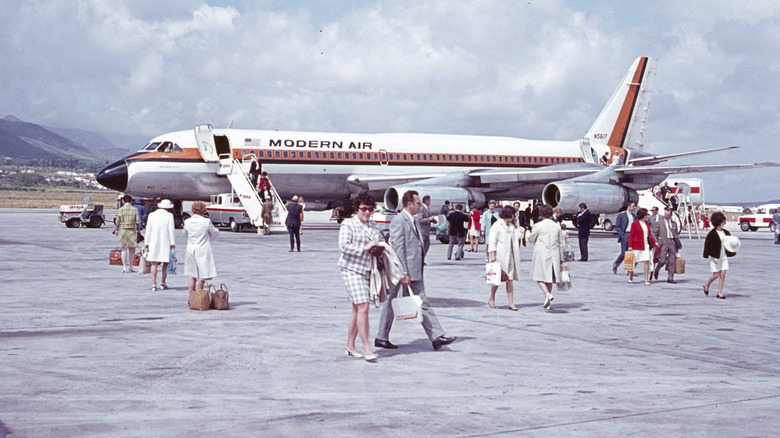 Travelers roam the tarmac in front of a Modern Air jet in the 1960s