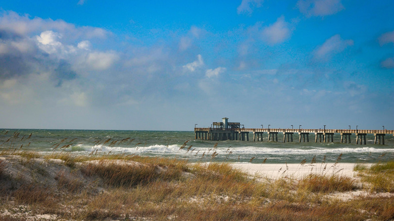 View of pier stretching into water with waves and blue sky