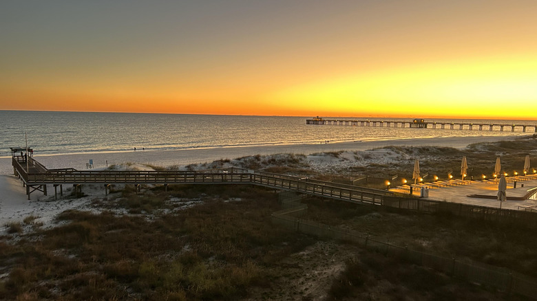 Sunset over the ocean, with wooden boardwalk leading to the shore and a pier stretching into the water, ﻿﻿Gulf State Park, Alabama
