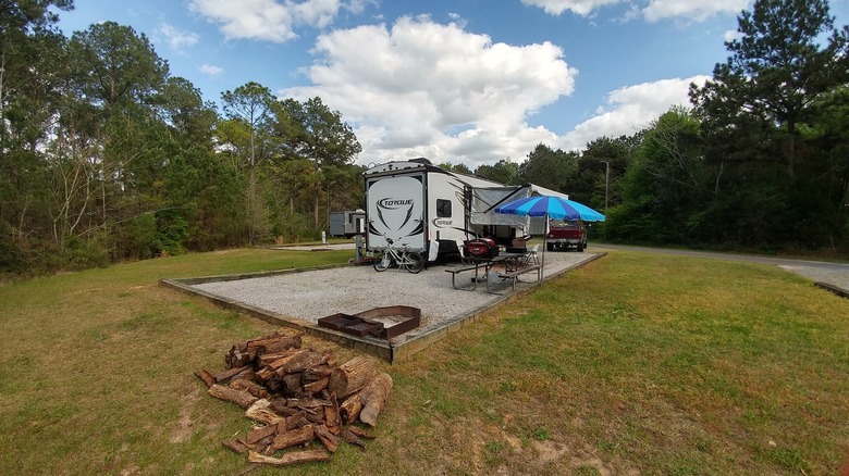 Spacious campsite at the Frank Jackson State Park campground, Alabama, with a parked trailer, picnic table, and firewood