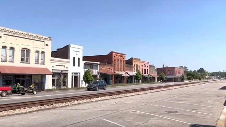 A screenshot from a video showing the downtown area of Brewton Alabama with storefronts and cars behind train tracks.