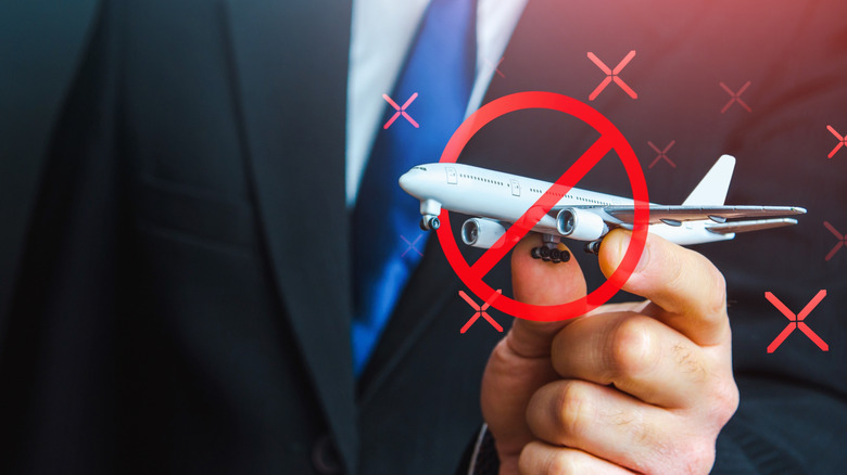 A man in a suit holding a model airplane with a cross through it, symbolizing canceled flights