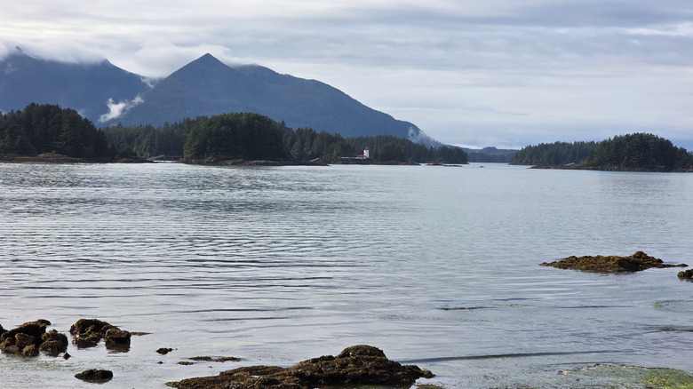 The Sitka Lighthouse by water, and tree-filled mountains in Sitka, Alaska