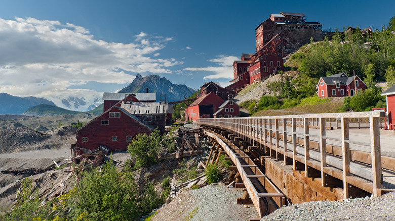 Old boardwalk traversing between abandoned red buildings against the dramatic Alaskan range in Kennecott