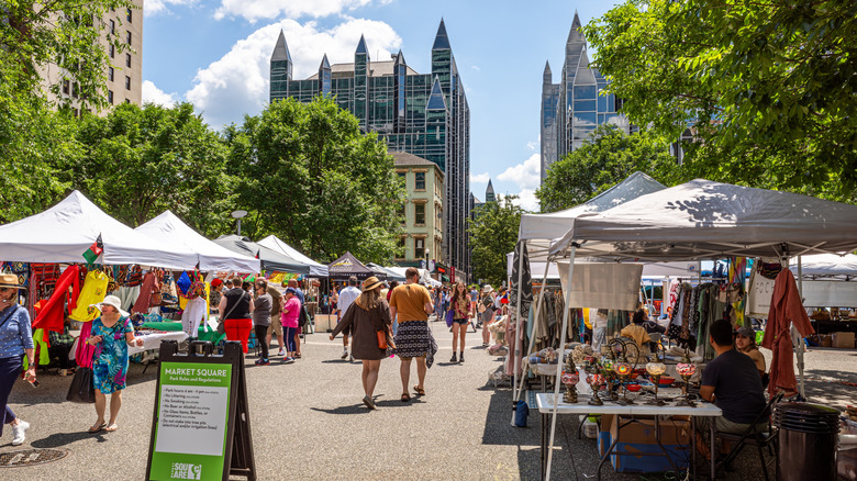 Market Square in Pittsburgh, with people walking between white festival tents surrounded by trees with the glass spires of the PPG Building in the background, under a cloudy blue sky
