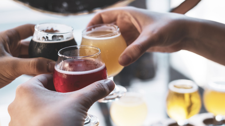 Three people toast each other with small glasses of beer.