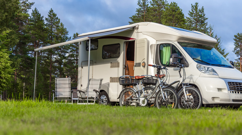 An RV with an awning and bicycles parked in a grassy field.