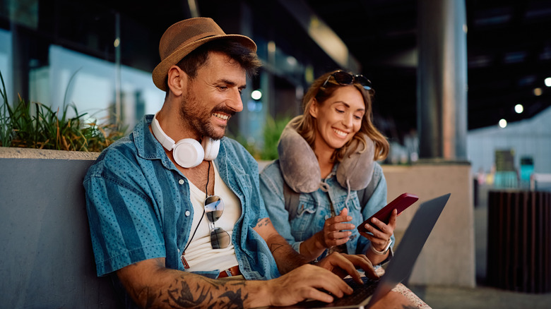 A couple with a laptop, phone, headphones, and other tech at an airport