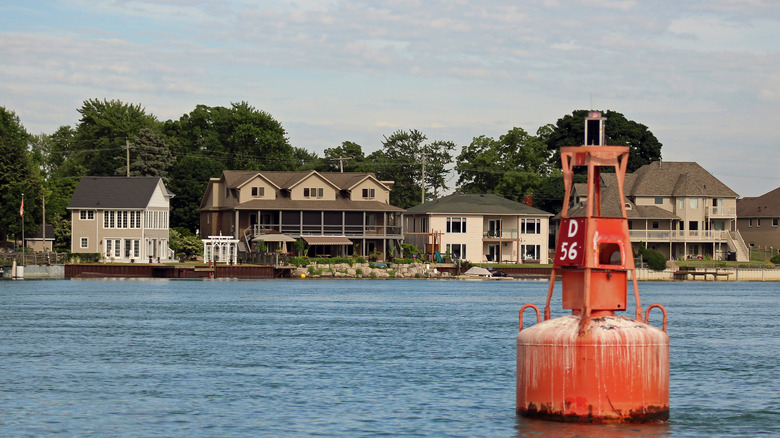 Beautiful riverfront homes in Amherstburg, Ontario, backgrounded by green trees with a buoy marker in the foreground.