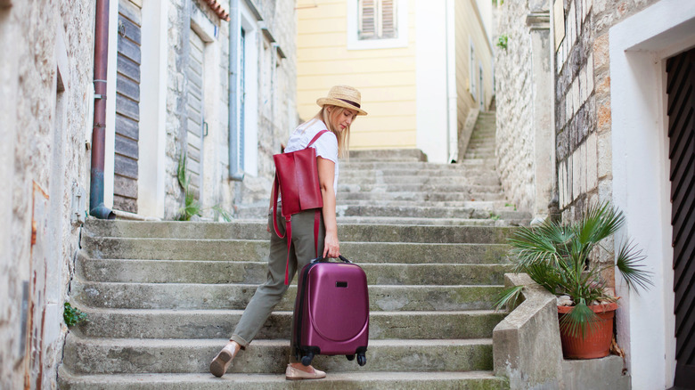 Person carrying roller suitcase up stairs