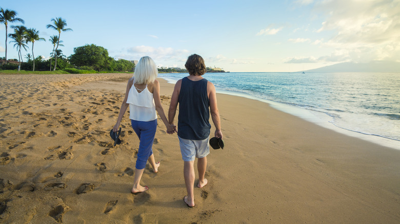 A couple walking hand-in-hand along a beach in Maui