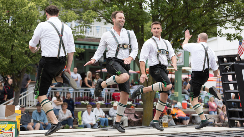 group of four Caucasian men in traditional German lederhosn dancing on a stage