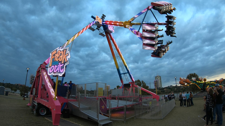 a lit up adventure sport ride with people swinging in the air, twilight sky