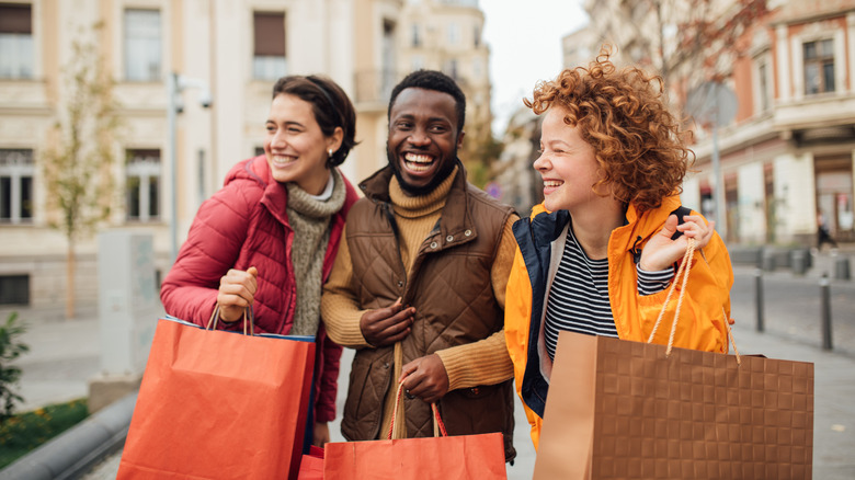 Three people laughing while holding shopping bags.