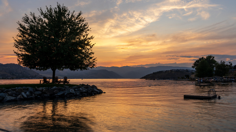 Dramatic sunset over Lake Chelan with silhouette of tree and chairs next to the smooth water of the lake in WA