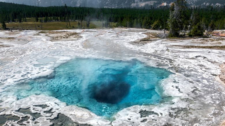 a fuming electric blue geyser pool in the center surrounded by white silica deposits