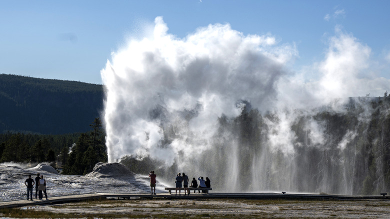 geyser vents a massive cloud of steam as visitors watch