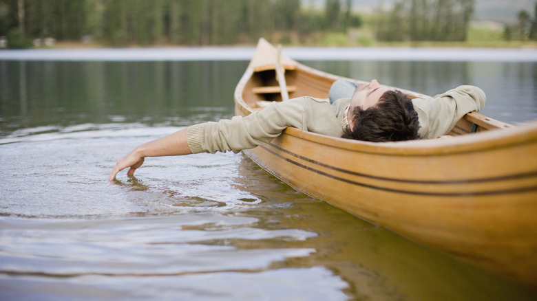 A man relaxing on a rowboat in the middle of a lake.
