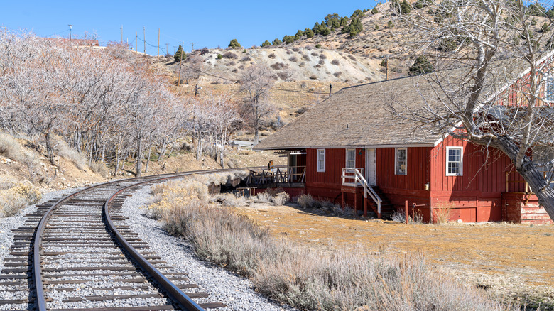 Train tracks winding near brown hills and a red cabin