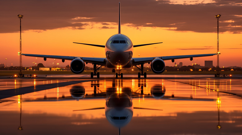 A commercial aircraft on a runway at an unidentified airport just after sunset, with warm evening light all around.