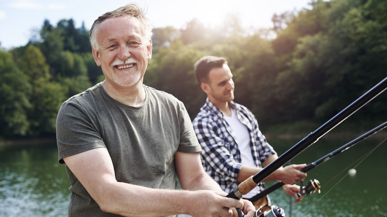 A smiling senior man fishes with a younger man.