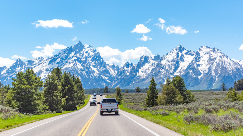 Rear shot of a car driving along a highway toward snowcapped mountains in the distance