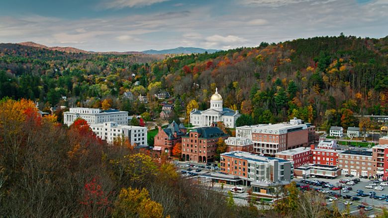 Red and white buildings nestled between two hills covered in red, orange and green fall foliage