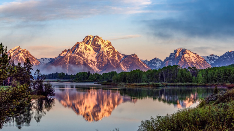 Mountains under golden hour reflected across a river's surface in the foreground