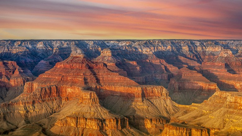 The orange-yellow striated rock walls and ravines of the Grand Canyon at sunset
